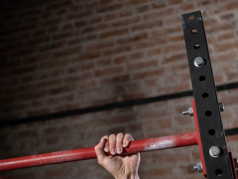 Close-up of a man's hands gripping a pull-up bar, showing focus and muscle tension.